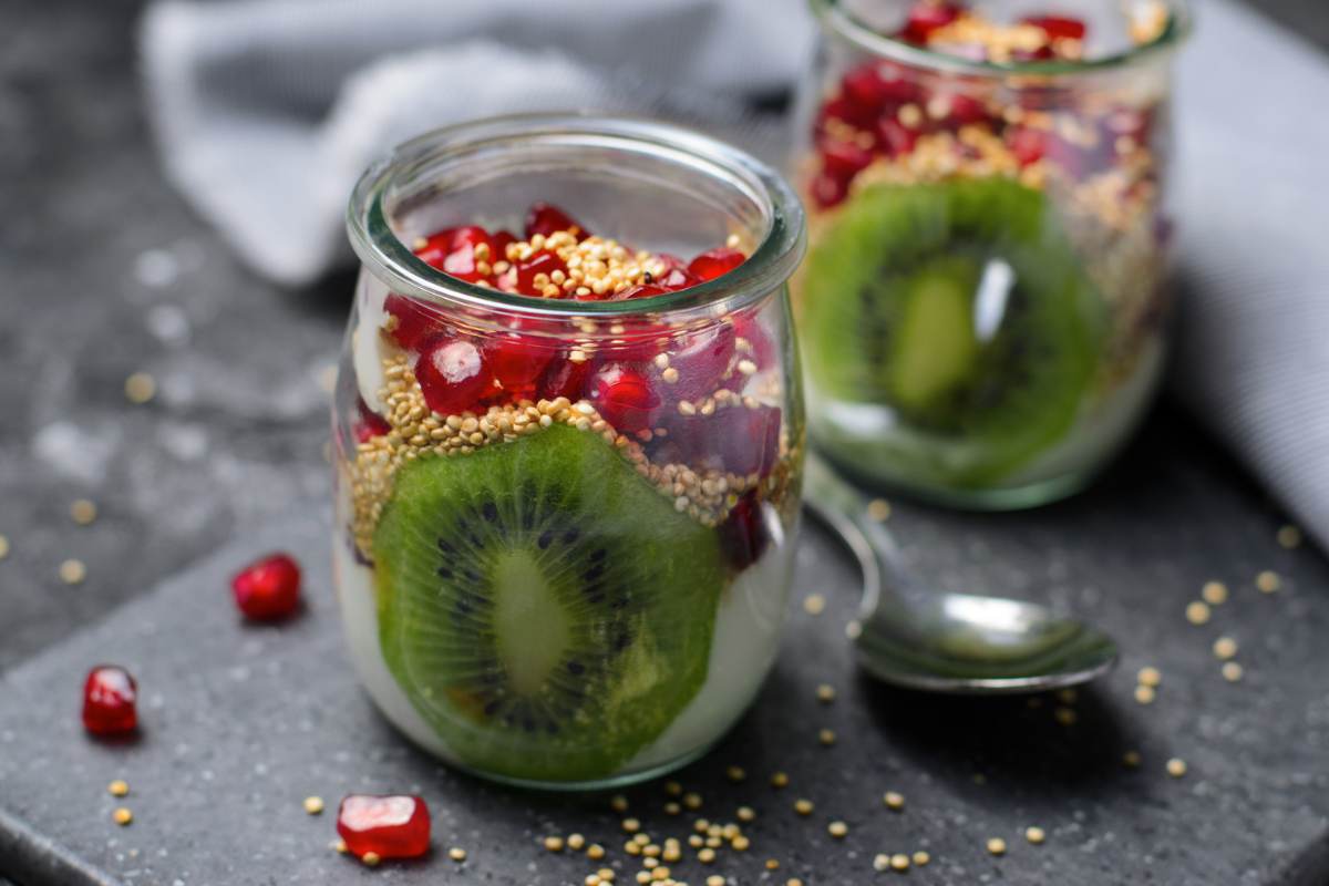 Pimp up your quinoa with this vibrant parfait featuring layers of fluffy quinoa, fresh kiwi slices, and juicy pomegranate seeds in a glass jar, garnished with scattered quinoa grains.
